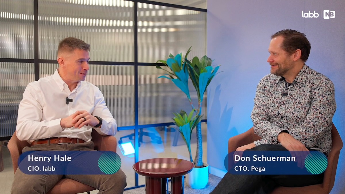 Video still of Henry Hales, CIO at labb and Don Schuerman, CTO at Pega sitting and speaking in a room with an internal obscured glass window behind them